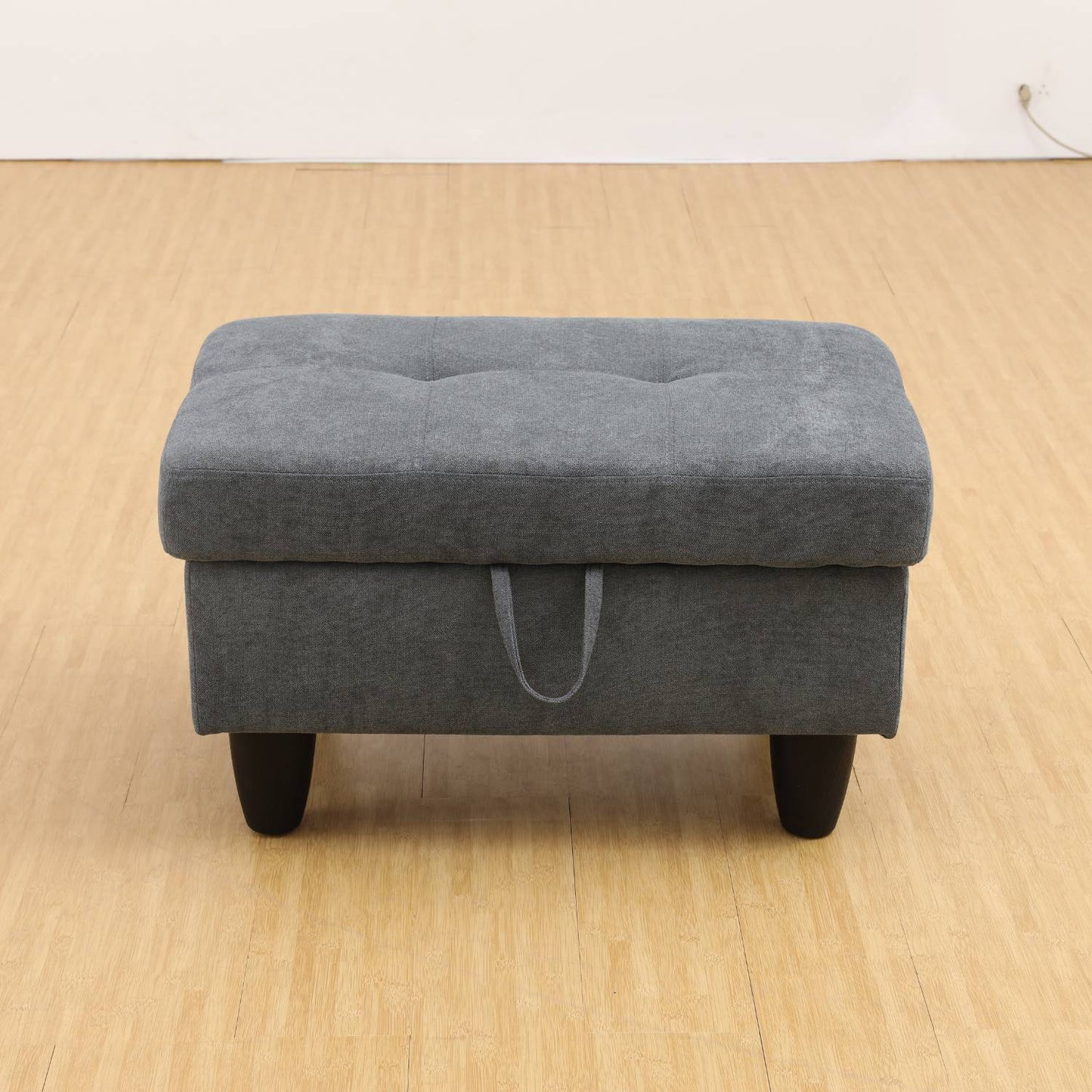 A dark grey flannel upholstered ottoman with a low-profile design and metal legs on a wooden floor.