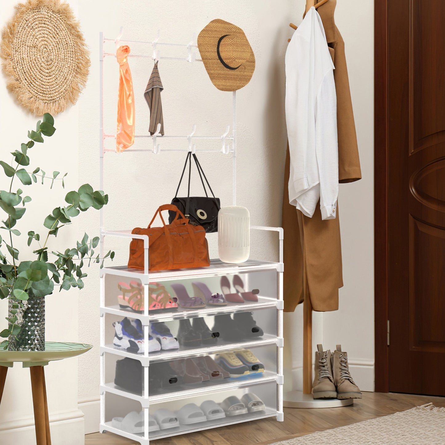 A white 5-tier shoe rack with coat rack, placed in an entryway with various items such as shoes, coats, and a bag organized on and hanging from it. The area is well-lit with natural light and there is a plant to the side.