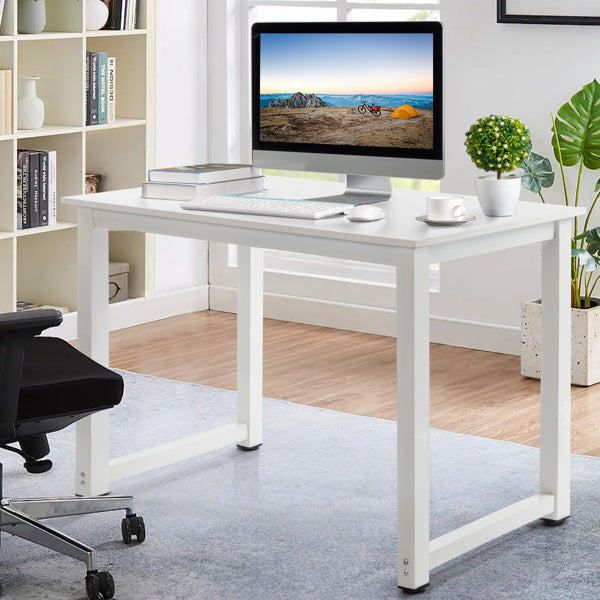 A modern white computer desk with a metal frame and engineered wood top, fitted with a monitor, keyboard, and a coffee cup, set in a room with bookshelves and a plant.
