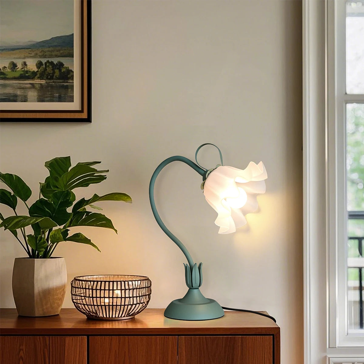 Teal table lamp on a wooden surface with a plant and bowl in a room setting.