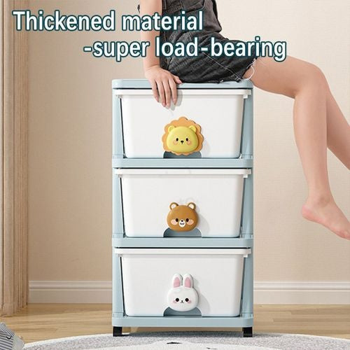 A child sitting on a storage drawer unit with three layers, featuring animal face designs on the drawer handles. The unit is white and blue in color and appears to be made of plastic.