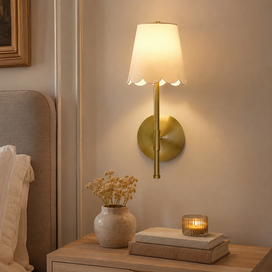 Cordless brass scalloped wall sconce styled beside a neutral bed