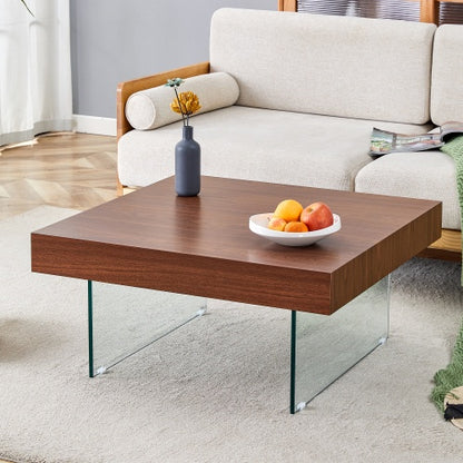 A walnut colored square MDF coffee table with tempered glass legs, placed in a living room setting with a bowl of fruits on top.