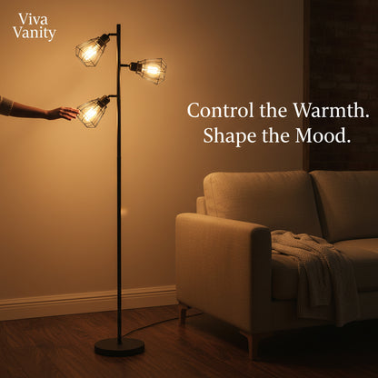 A floor lamp with a metal cage shade, standing between two gray armchairs in a room with a striped rug and a framed picture on the wall.