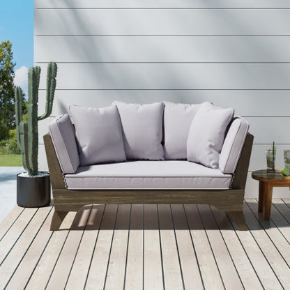 A gray fabric sofa bed on a wooden frame with a slatted panel, placed on an outdoor patio next to a potted cactus.