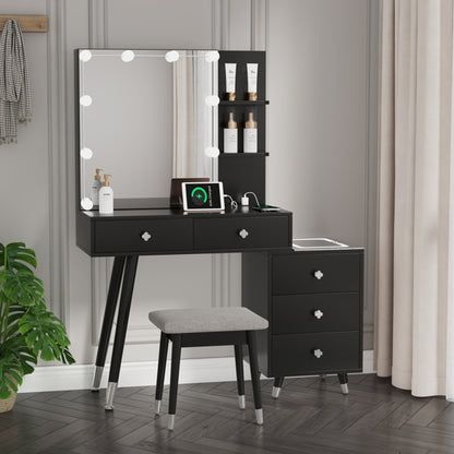 A modern black luxury dressing table set with an LED mirror, multiple storage drawers, and a cushioned stool. The set is placed in a room with light gray walls and curtains.