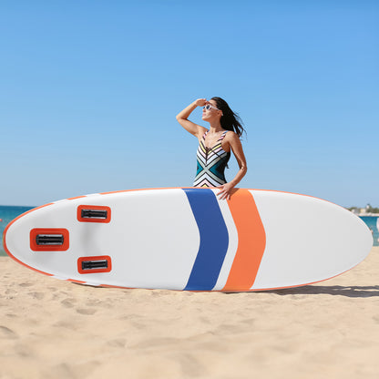 Woman holding a colorful surfboard on a sandy beach with clear blue sky.