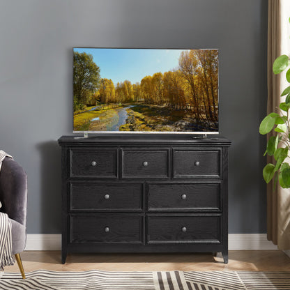 A black, handleless seven-drawer fiberboard vanity with an extended tabletop, situated in a well-lit room with a flat-screen TV on top displaying a nature scene, placed against a gray wall with a potted plant to the side.