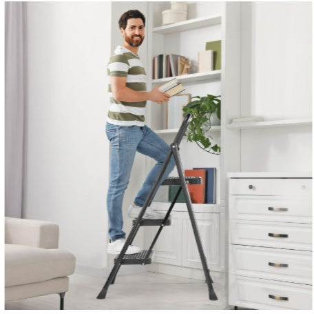 Man using a step ladder to reach items on a high shelf in a room with white walls and furniture.
