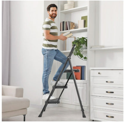 Man using a step ladder to reach items on a high shelf in a room with white walls and furniture.