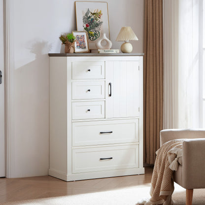 A white and gray farmhouse style 5-drawer dresser with a dressing table on top, placed in a room setting with a chair and decorative items.
