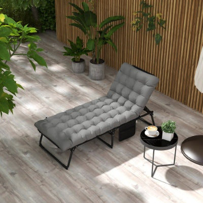 An adjustable folding chaise lounge in gray color with a tufted cushion, placed on an outdoor setting with plants and a small table beside it.