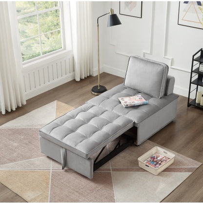 A gray velvet convertible sofa bed with a magazine on it, retracted into a flat bed position, shown in a room setting with a lamp and a side table.