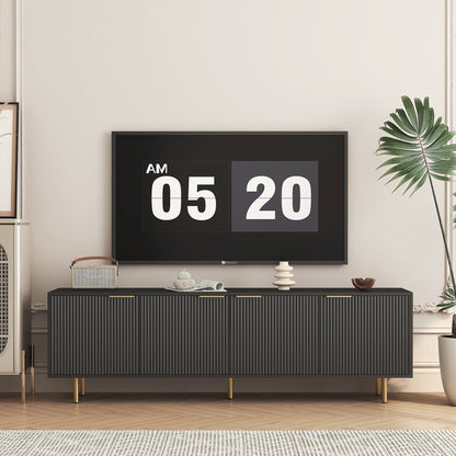 A modern black TV stand with fluted doors and gold legs, featuring a digital clock on the wall and decorative items on the top surface.