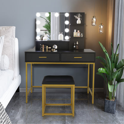 A modern minimalist three-tier dressing table set with a black particleboard tabletop and steel frame, featuring dual soft-close drawers and three open display tiers, accompanied by a black padded stool and decorative items on the table surface, placed in a room with a potted plant and a wall mirror.