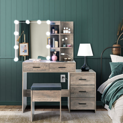 A dressing table set with 3 drawers, featuring a mirror and stool. The table is placed against a wall with paneling, and there is a bed with green bedding in the background.