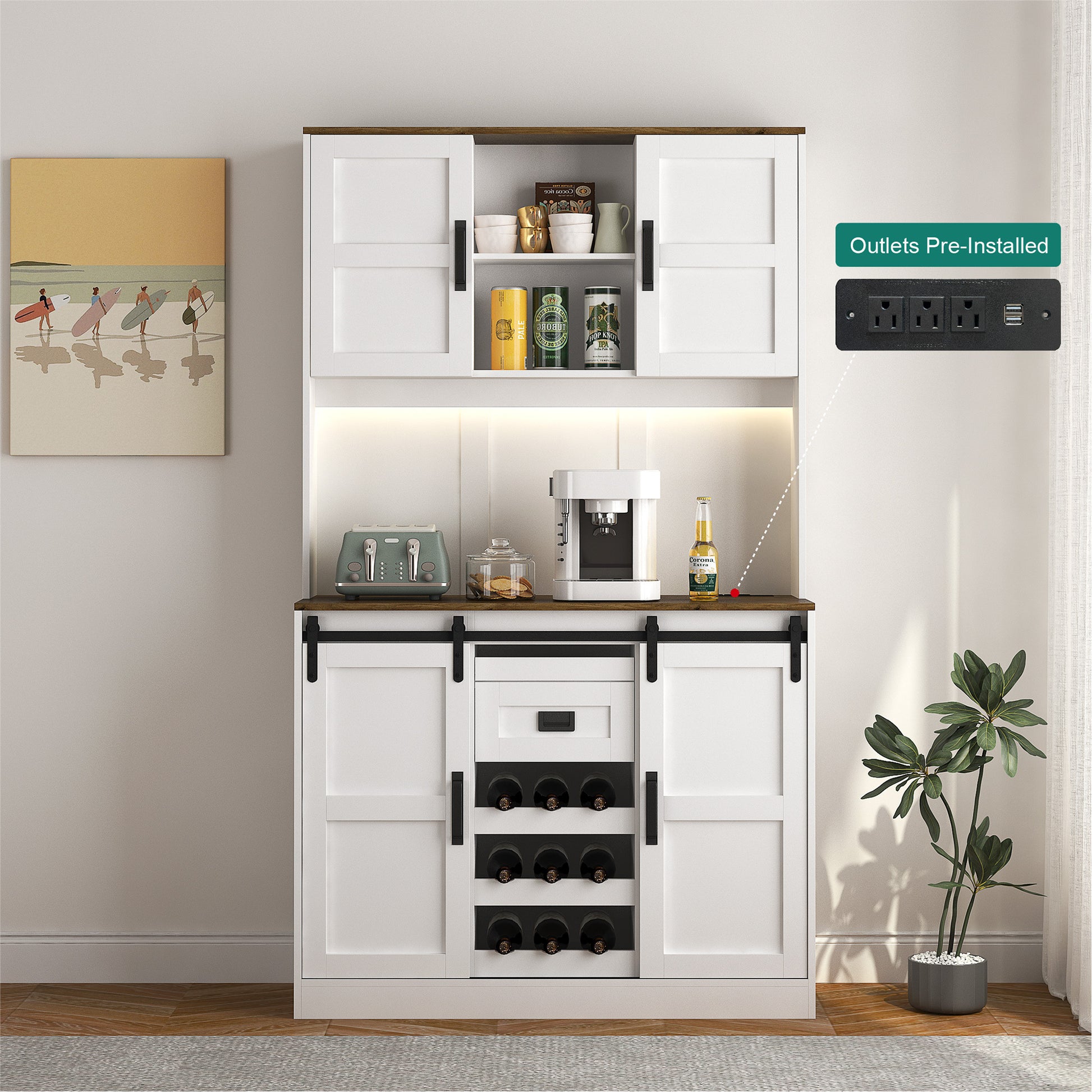 A white bar cabinet with sliding barn doors and a countertop, integrated with a power strip for electrical appliances. It is positioned against a wall with a decorative painting and next to a potted plant.