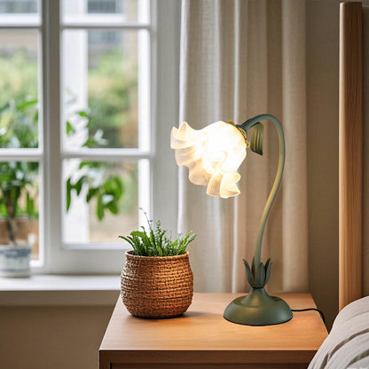 Decorative table lamp with a plant on a wooden surface near a window.