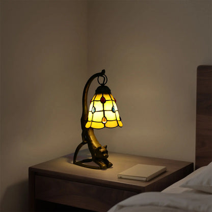 Decorative lamp with stained glass shade on a nightstand next to a bed.
