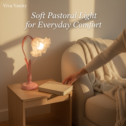 Pink desk lamp with floral design on a white surface next to a vase with flowers.