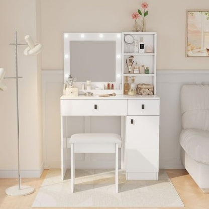 A white vanity desk with a mirror and lights, featuring three large drawers and a small bench. The vanity is placed in a bedroom setting with a floor lamp to the side.