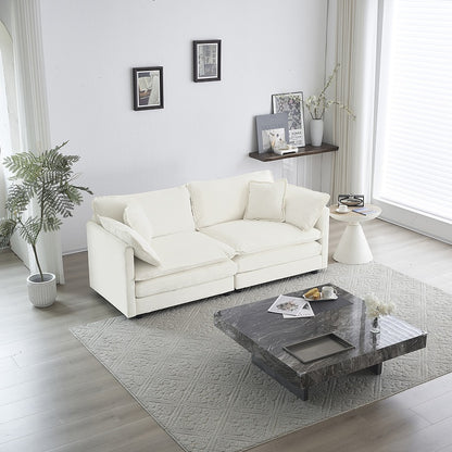 A modern white fabric loveseat sofa with four pillows, placed in a bright living room setting.