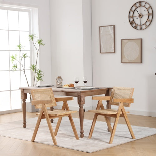 A set of two beige upholstered armchairs with solid wood legs and a wooden dining table, placed in a well-lit room with neutral wall decor.