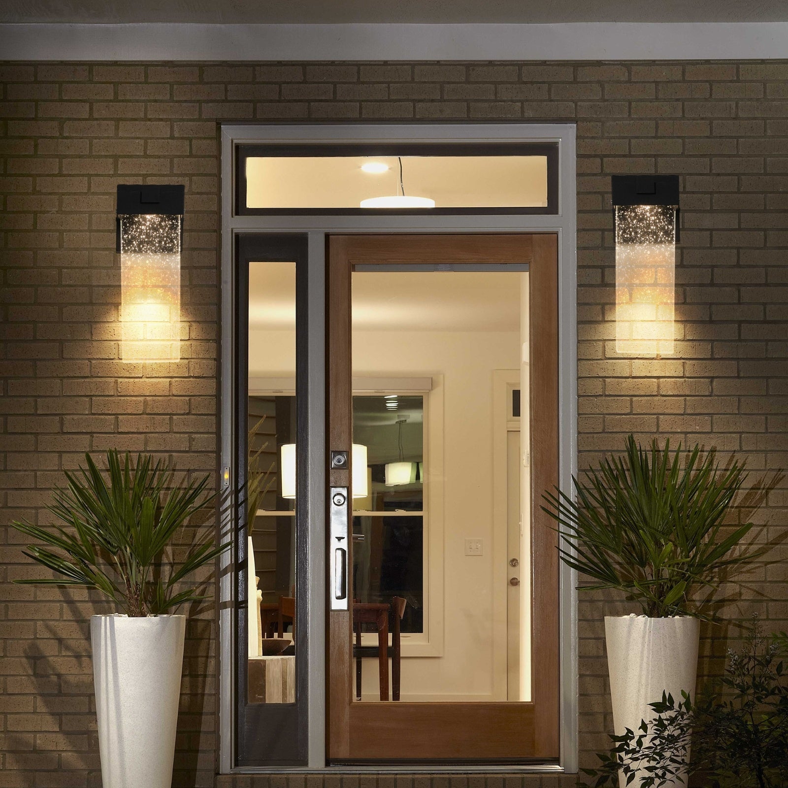 Modern front door with glass panels on a brick wall, illuminated by outdoor lights.