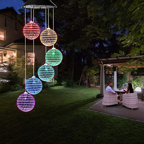 Colorful spherical lights hanging above a garden with people sitting at a table.