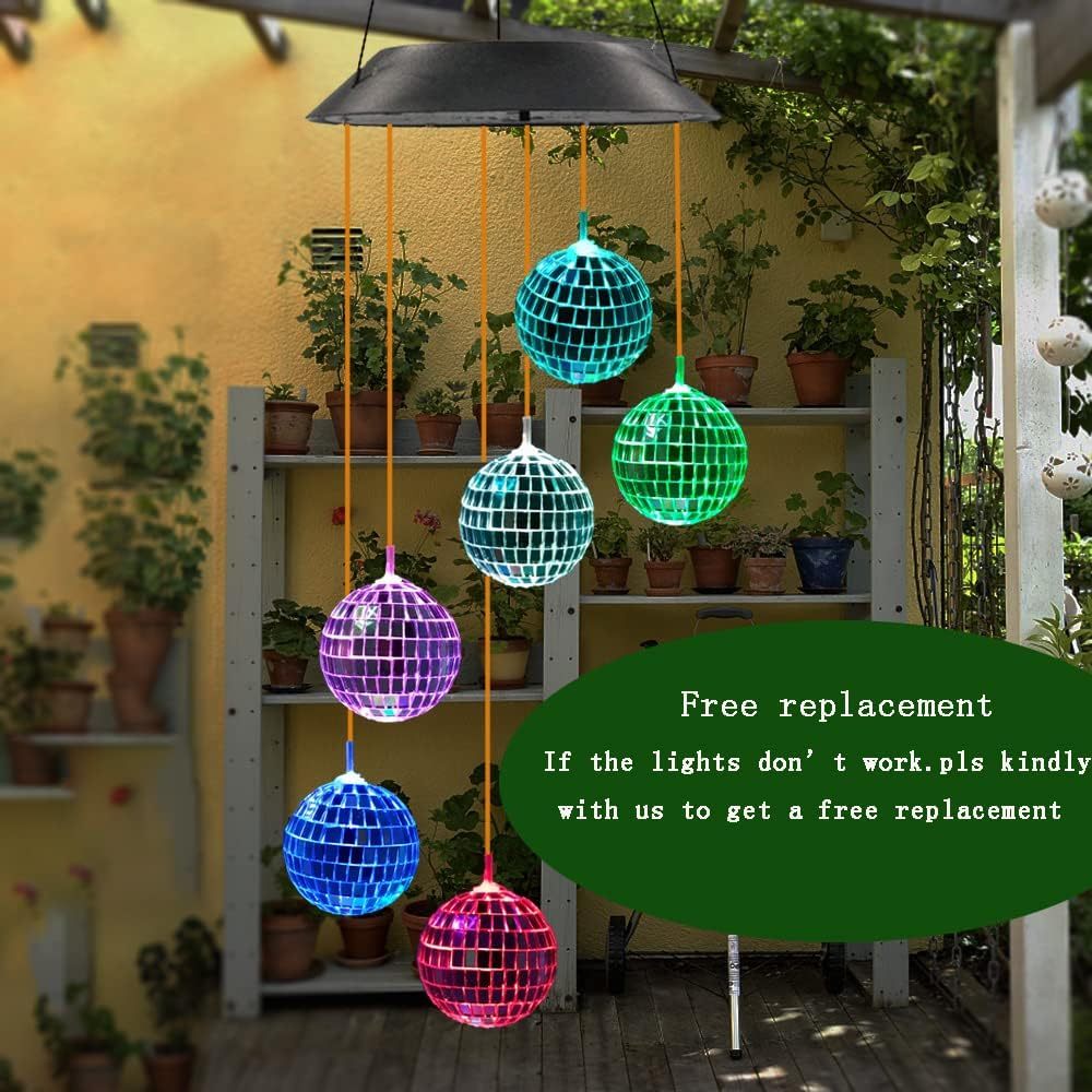 Colorful disco ball wind chime hanging outdoors with plants and shelves in the background.