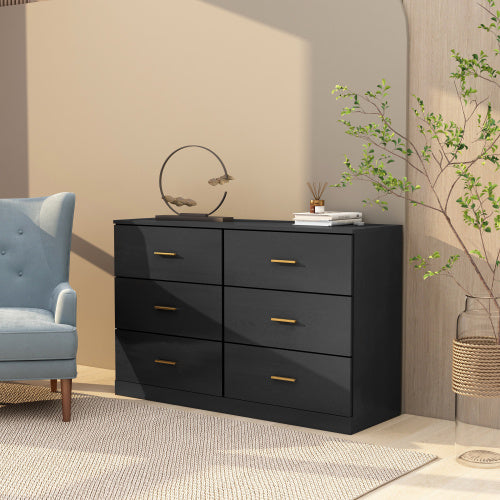 A matte black six-drawer bedroom vanity with brushed nickel metal pulls, placed in a well-lit room with a chair and decorative items on top.