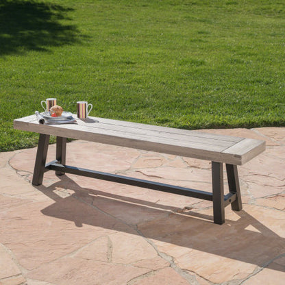 Acacia wood dining bench with a black rustic metal frame, placed on a stone surface with grass in the background.