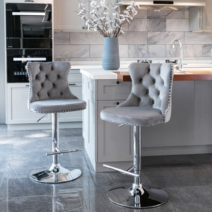 Two gray upholstered swivel barstools with tufted backrests and adjustable chrome bases, placed in a kitchen setting.